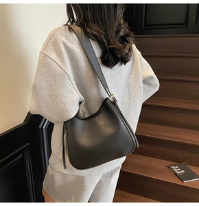 Close-up of a black matte soft leather hobo bag worn by a model on wooden stairs