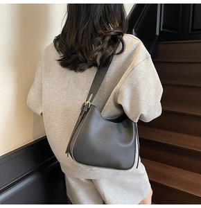 Detail of minimalist black leather hobo bag with gold buckle and tassel on shoulder strap