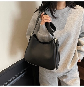 Detail of minimalist black leather hobo bag with adjustable gold buckle and wide strap