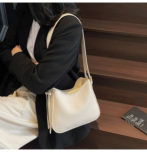 Close-up of cream-colored hobo bag with tassel detail and gold hardware on model