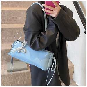 Detail of light blue patent leather bag with pearl bow and silver heart charm