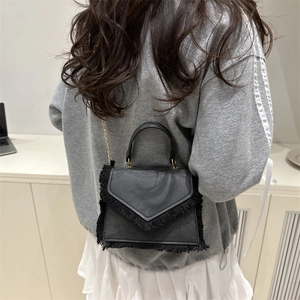 Fashionable black crossbody bag with fringe detail and gold chain shown on a model