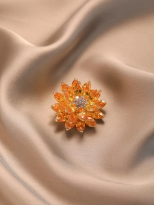 Détail d'une broche lotus à trois niveaux avec zircons ambrés sur satin champagne