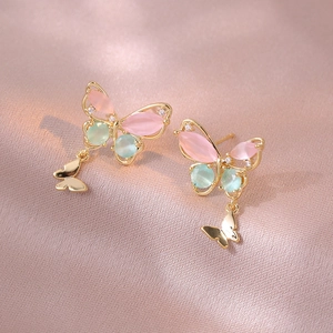 Elegant butterfly stud earrings with pink and green stones on pink satin fabric