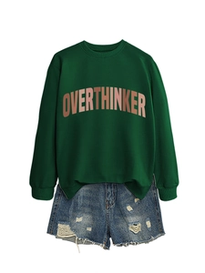 Detail of OVERTHINKER print on dark green crewneck sweatshirt with distressed denim shorts