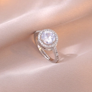 Silberner Halo-Ring mit großem Zirkonia und Pavé-Kristallen auf einem Satinhintergrund