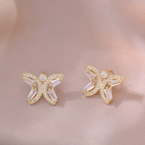 Detail of golden butterfly stud earrings featuring micro-pave crystals on satin fabric