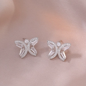 Detailed close-up of silver butterfly stud earrings with zircon inlay on pink fabric