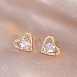 Elegant gold-plated hollow heart earrings with large zircon center on silk background