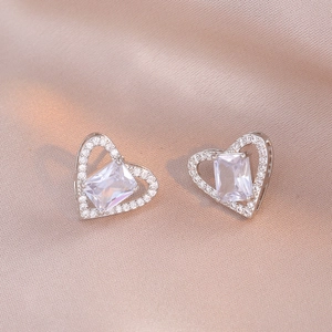 Macro shot of silver heart earrings with rectangular zircon center on silk background