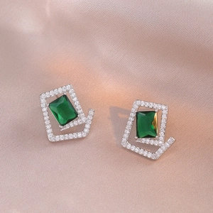 Macro shot of geometric earrings with emerald green stones on silk background