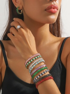 Close-up of stacked colorful marquise-cut zircon bangles and emerald earrings on model