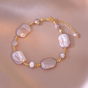 Detail of baroque pearl bracelet with purple luster and gold beads on pink satin fabric