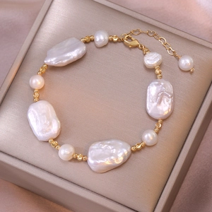 Detailed shot of baroque pearl bracelet with gold beads on champagne silk background