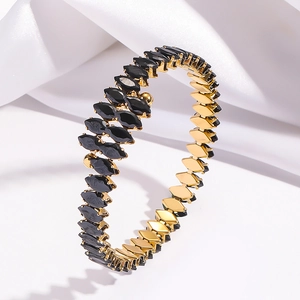 Macro view of gold bracelet with marquise-cut black stones on white silk background