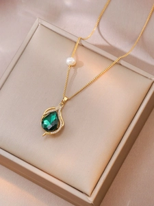 Detail of gold necklace featuring teardrop emerald pendant and white pearl on silk box