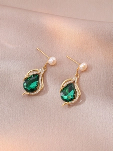 Close-up of pearl drop earrings with pear-cut green zircon on champagne silk cloth