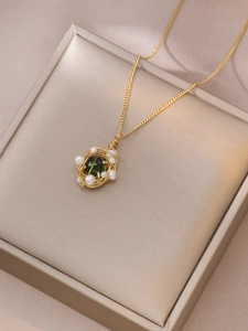 Détail du pendentif nid d'oiseau doré avec perle vert émeraude et perles blanches