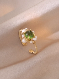 Détail macro d'une bague artisanale en fil doré avec pierre verte et petites perles