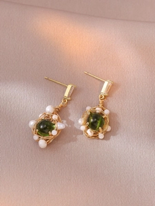 Détail de boucles d'oreilles dorées avec pierres vertes et perles sur satin de soie