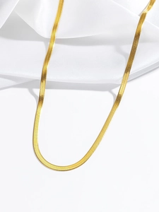 Détail d'un collier en maille serpent dorée posé sur un tissu en soie blanche
