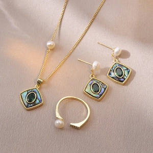 Flat lay of vintage gold jewelry set with abalone shell, green gems and pearls on silk