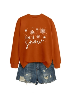 Flat lay of an orange crewneck sweatshirt with Let It Snow print and ripped denim shorts