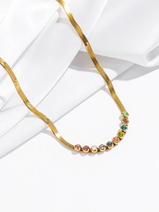 Detail of colorful round zircons on a gold snake chain necklace over white silk fabric