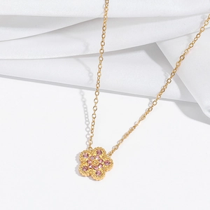 Detail of a gold floral pendant necklace featuring pink crystals on white silk background