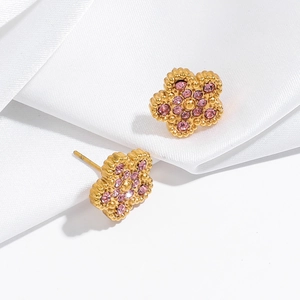 Macro view of gold-tone pink rhinestone clover flower earrings on white silk