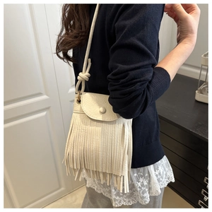 Close-up detail of beige leather crossbody bag with long fringe and bohemian knot strap