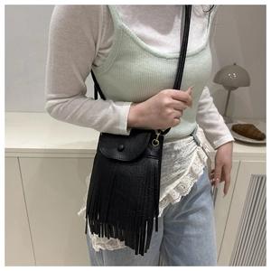 Close-up of black fringe crossbody bag with leather texture shown on model