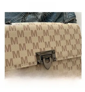 Close-up of cream shoulder bag with brown M patterns and vintage metal twist lock