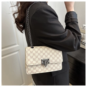 Detail of cream crossbody bag with brown M patterns and golden chain strap for women