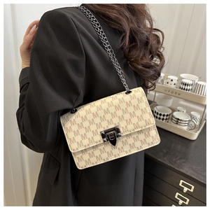 Detail of cream shoulder bag with M-letter print and black metal chain strap on a model