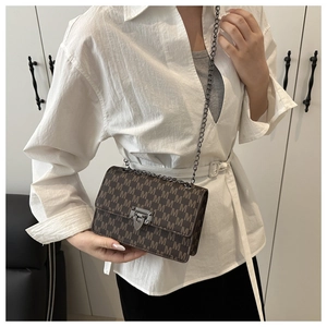 Detail of a brown leather shoulder bag with M-pattern print and a gold chain strap