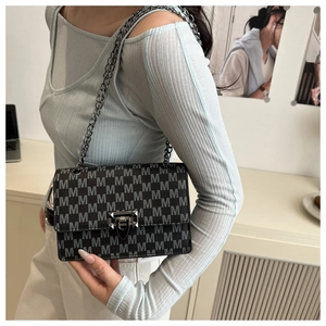 Black monogram crossbody bag with silver chain strap worn by a model in a modern room