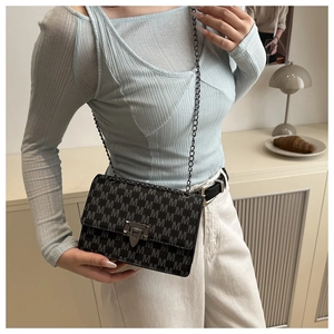 Close-up of black crossbody bag with M-pattern logo and metallic chain strap on a model