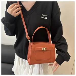 Detail of orange cross-grain leather handbag featuring a golden turn-lock closure