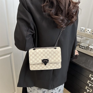 Chic beige crossbody bag with brown M-pattern and black chain strap worn with blazer