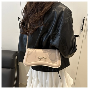 Close-up of cream white handbag featuring a sleek silver metal bow and fine leather texture