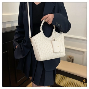 White monogram bucket tote bag with matching charm accessory worn by model in navy suit