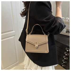 Chic beige leather shoulder bag with gold oval clasp shown on a model in a home setting