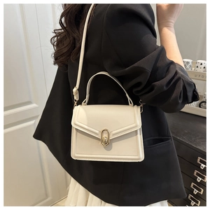 Crossbody view of a minimalist cream leather handbag with gold metal clasp on a black blazer