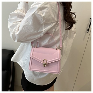 Detail view of a pink flap handbag with golden lock worn by a model in a white shirt