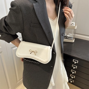White faux leather crossbody bag with golden bow clasp shown on a model in a grey suit