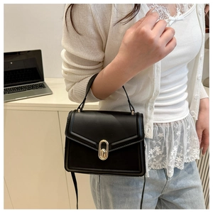 Close-up of golden oval twist lock and glossy leather texture on a black crossbody bag