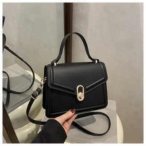 Detail of black matte leather handbag featuring a polished gold oval twist lock closure