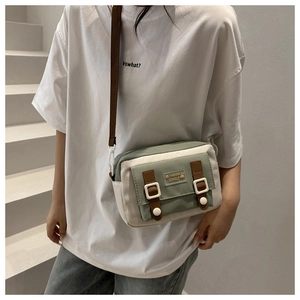 Détail du sac bandoulière en toile avec design bicolore vert et crème et sangles brunes