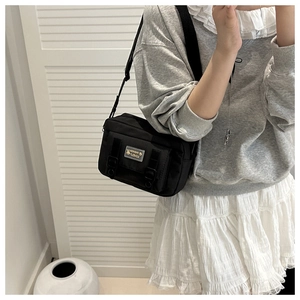 Détail du sac bandoulière compact en nylon noir avec boucles et patch mode logo